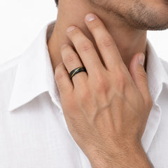 A close-up of a man wearing a slim black ring with a green inlay on his ring finger, wearing a white collared shirt against a clean white background.