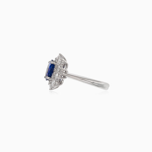 Klassischer Damenring aus 18 Karat Weißgold mit einem blauen Saphir im Ovalschliff und einem Halo aus Diamanten im Brillantschliff.