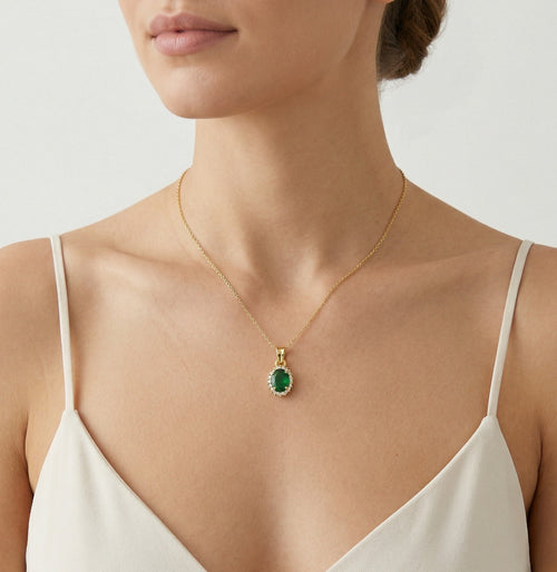 Oval cut emerald pendant with halo of cubic zirconia in yellow gold